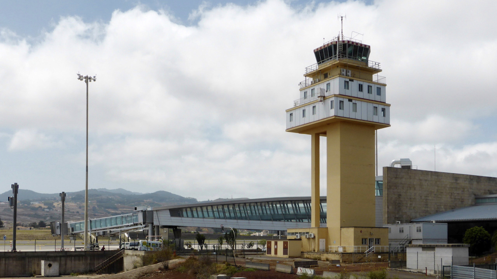 A picture of a yellow air traffic control tower, with white clouds in the background.